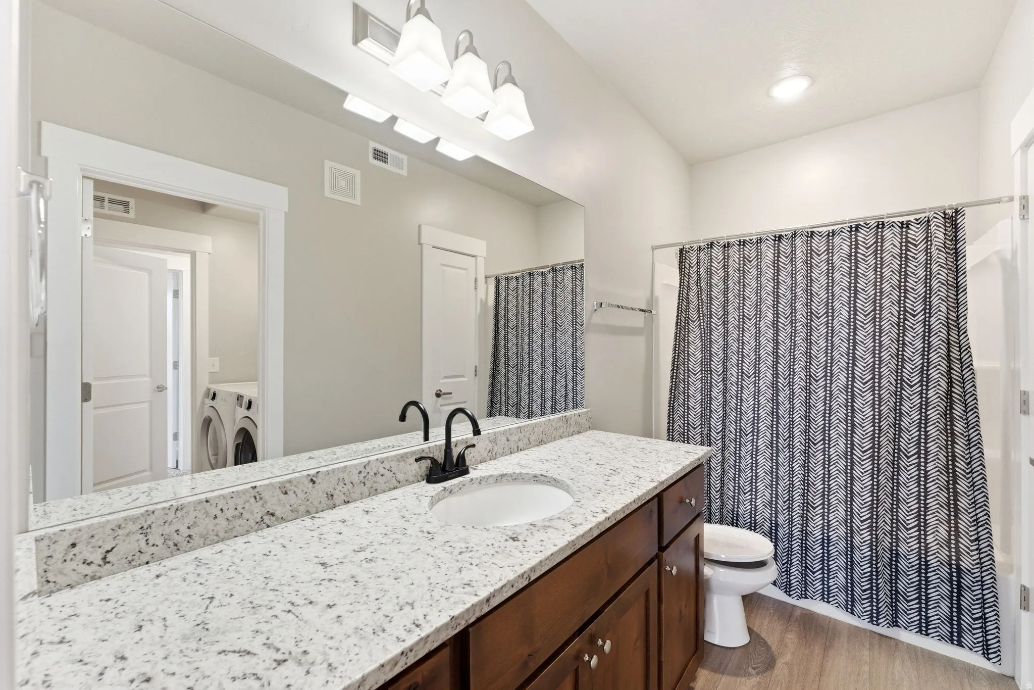 Bathroom featuring a dark wood-finish vanity with an undermount sink, a light speckled countertop, and matte black fixtures