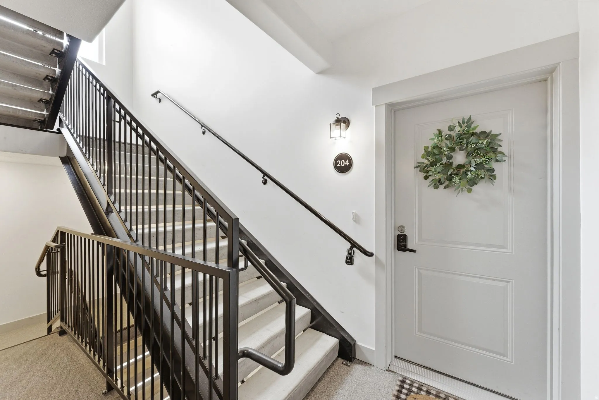 Stairwell featuring metal railings, light-toned stair treads, and a white entry door with panel detailing