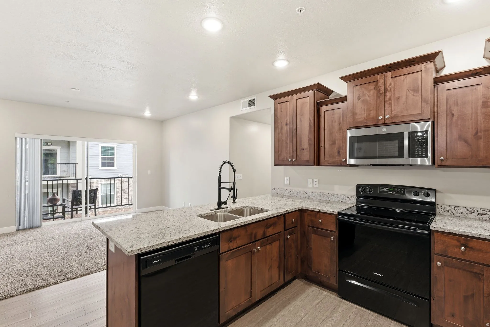 Modern kitchen featuring dark wood cabinetry, light speckled countertops, and stainless steel appliances including an oven, microwave, and dishwasher