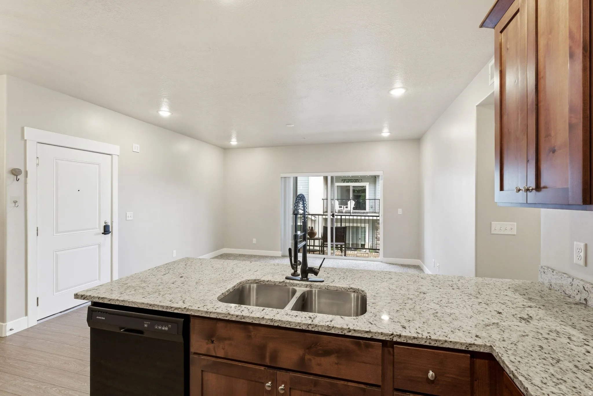 Kitchen island with light-toned granite countertops, a double basin stainless steel sink, and a matte black gooseneck faucet