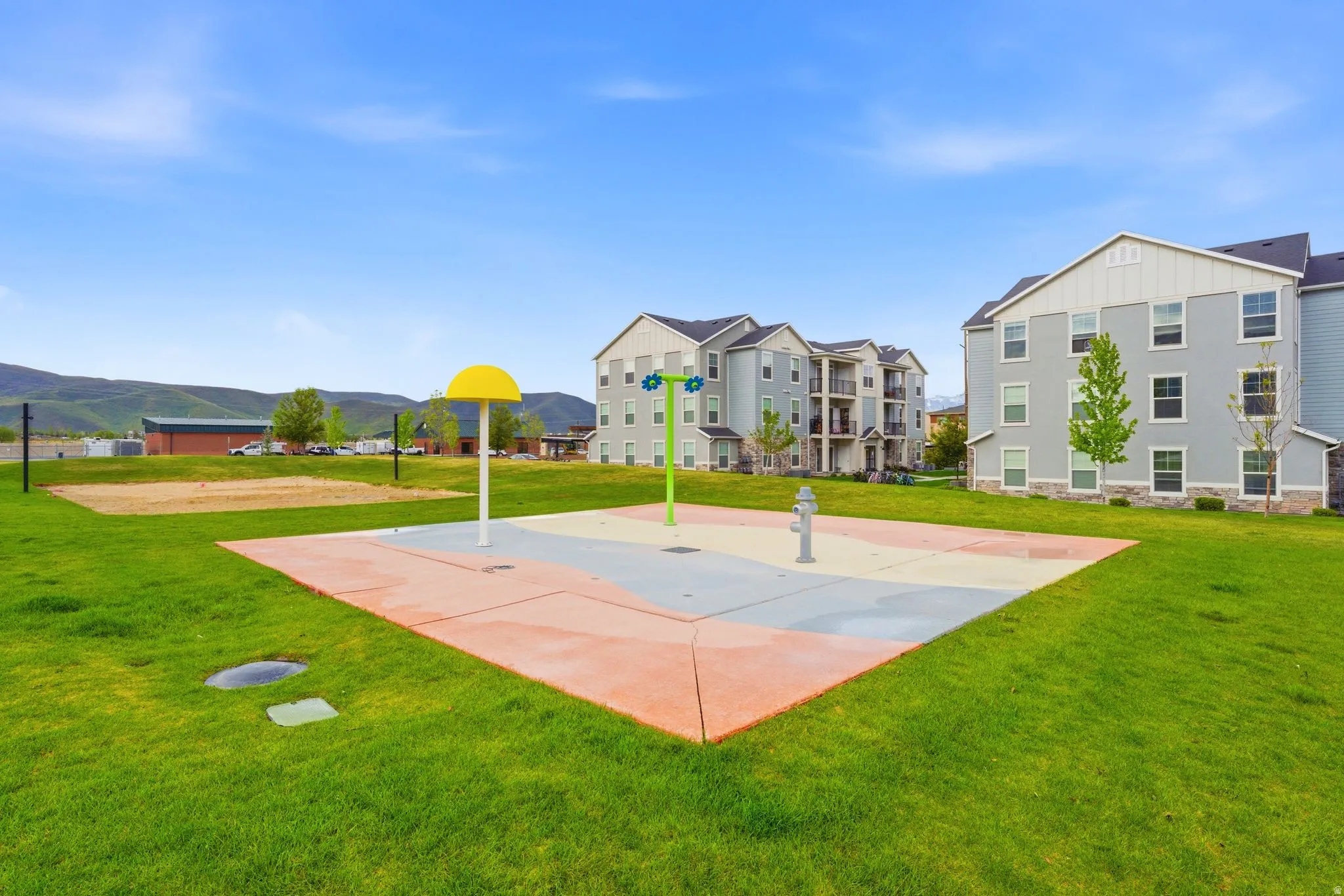 Recreational splash pad with colorful surfacing, surrounded by manicured green space
