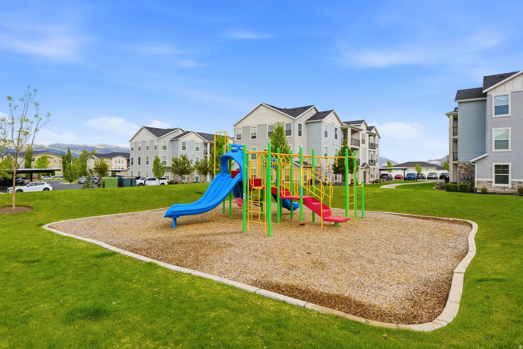 Community playground featuring a blue slide, red slide, and climbing structures on a wood chip base