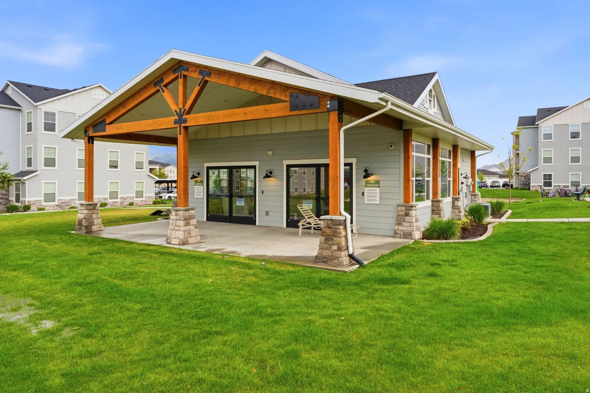 Craftsman-style clubhouse featuring a covered patio, exposed wood beams, stone column bases, and expansive glass doors