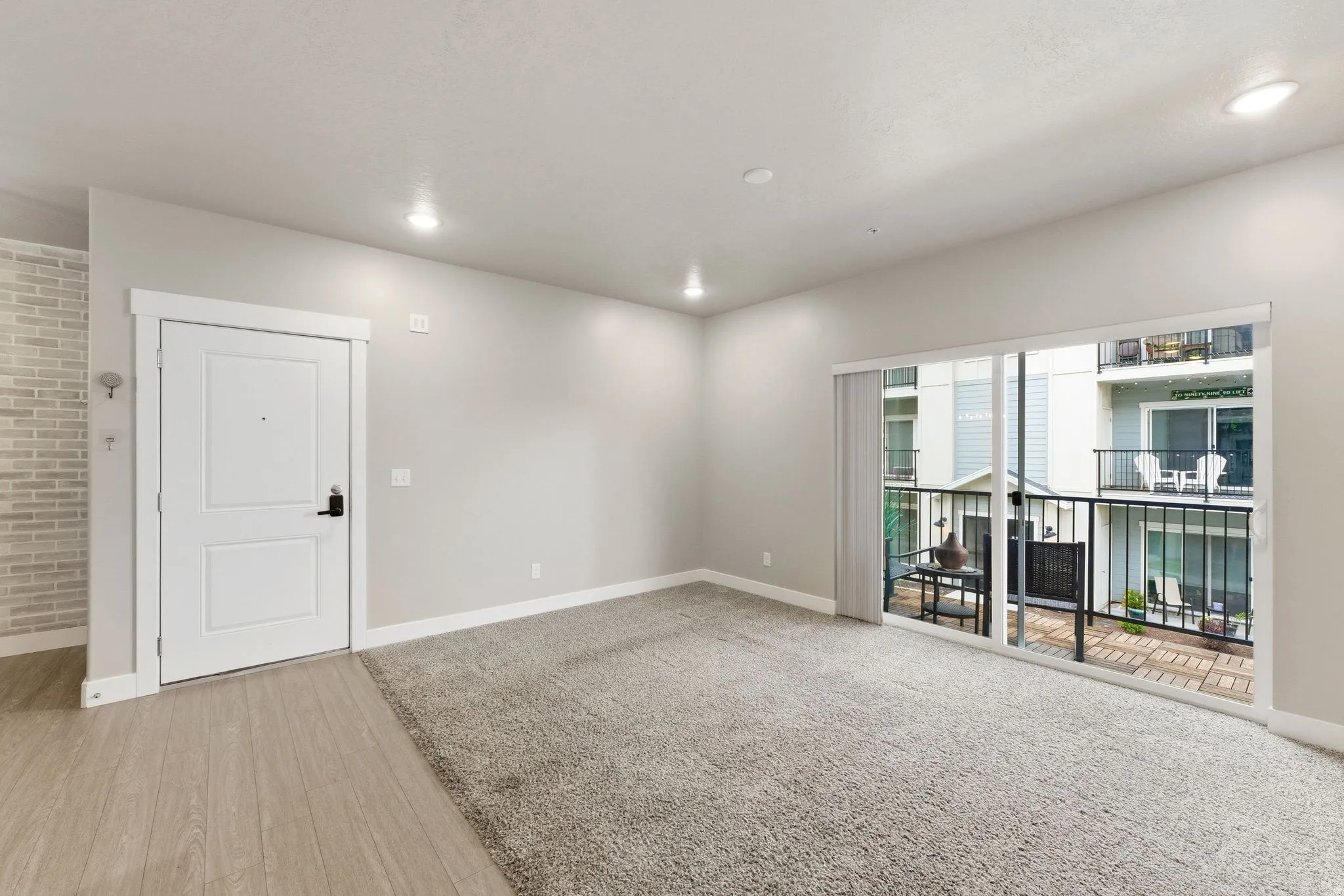 Living area with light gray walls, recessed lighting, and a combination of light wood-finish flooring and gray carpeting