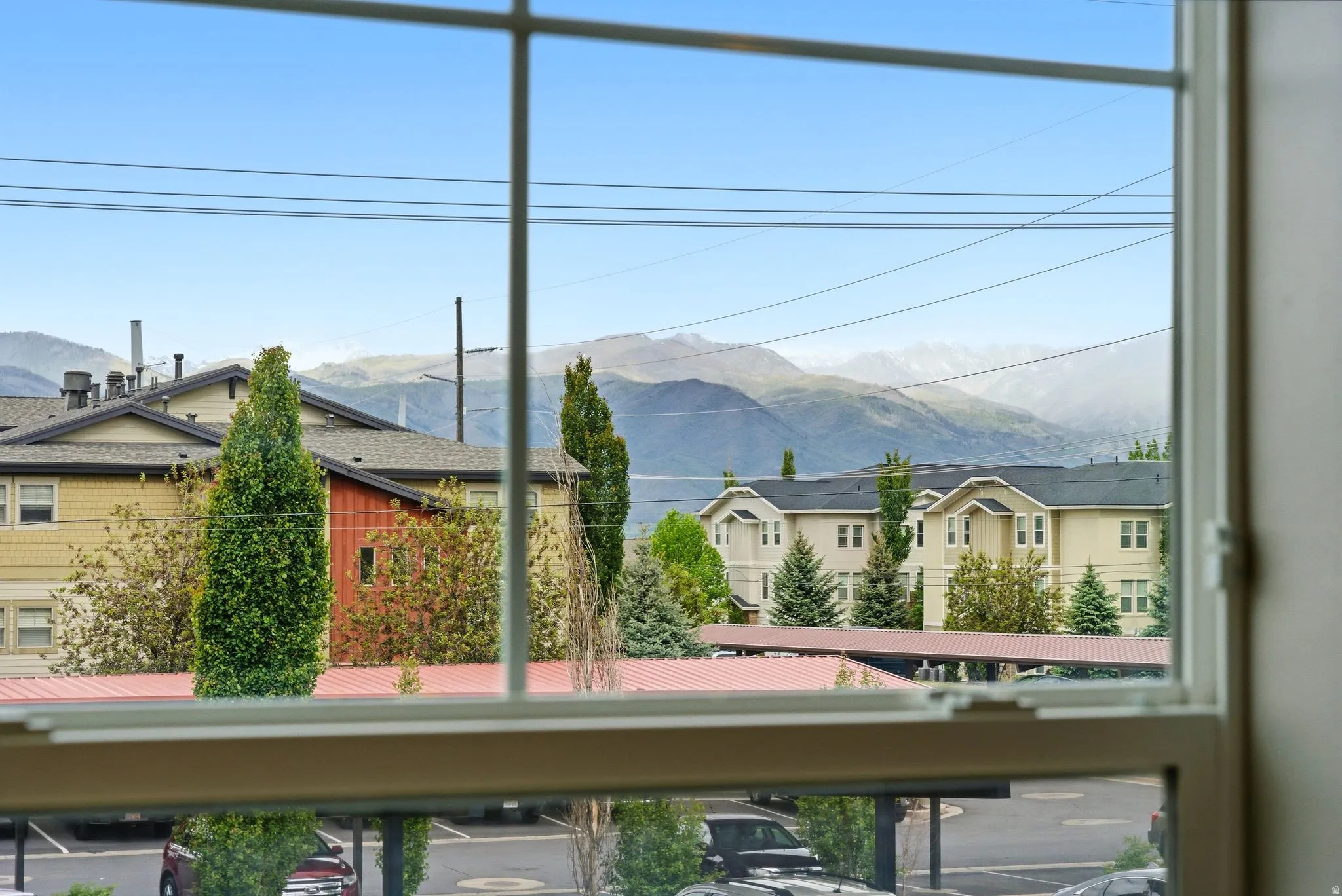 White framed window overlooking distant mountains, residential buildings, and covered parking structures