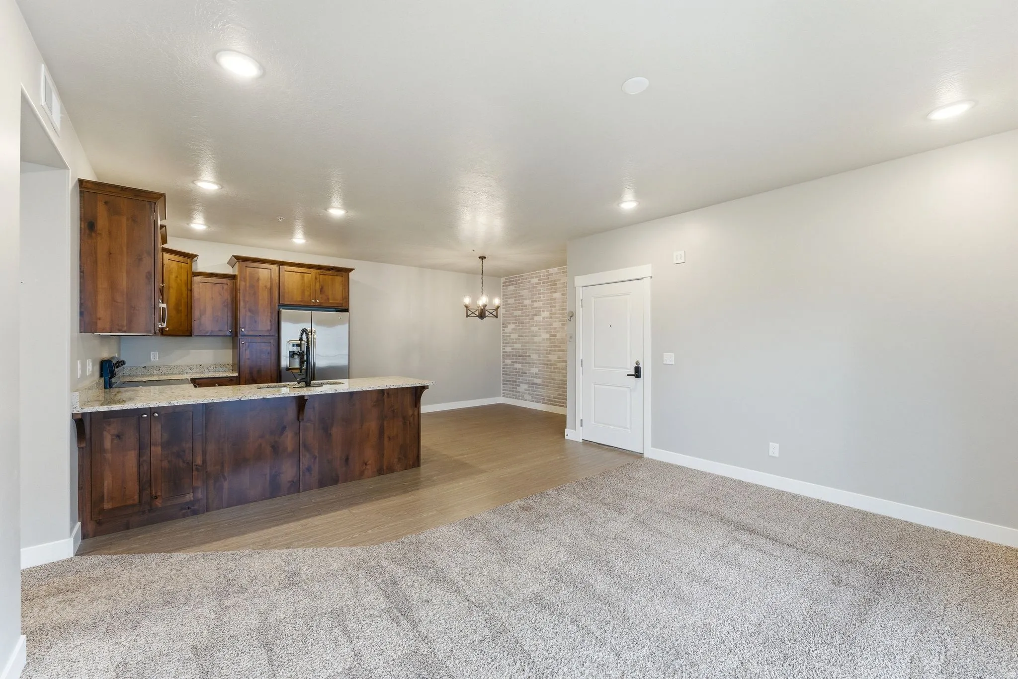 Open concept living space featuring a carpeted area, wood-finish flooring, and a kitchen with wood cabinetry, light-colored countertops, and stainless steel appliances