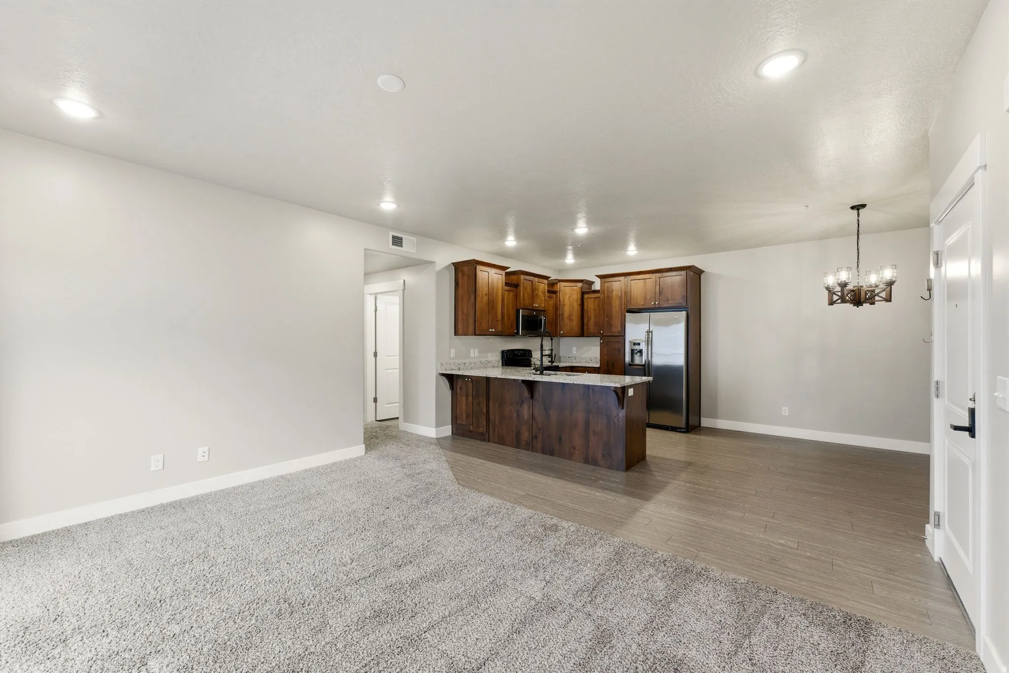 Open-concept living area featuring a kitchen with wood cabinetry, stainless steel appliances, and a breakfast bar