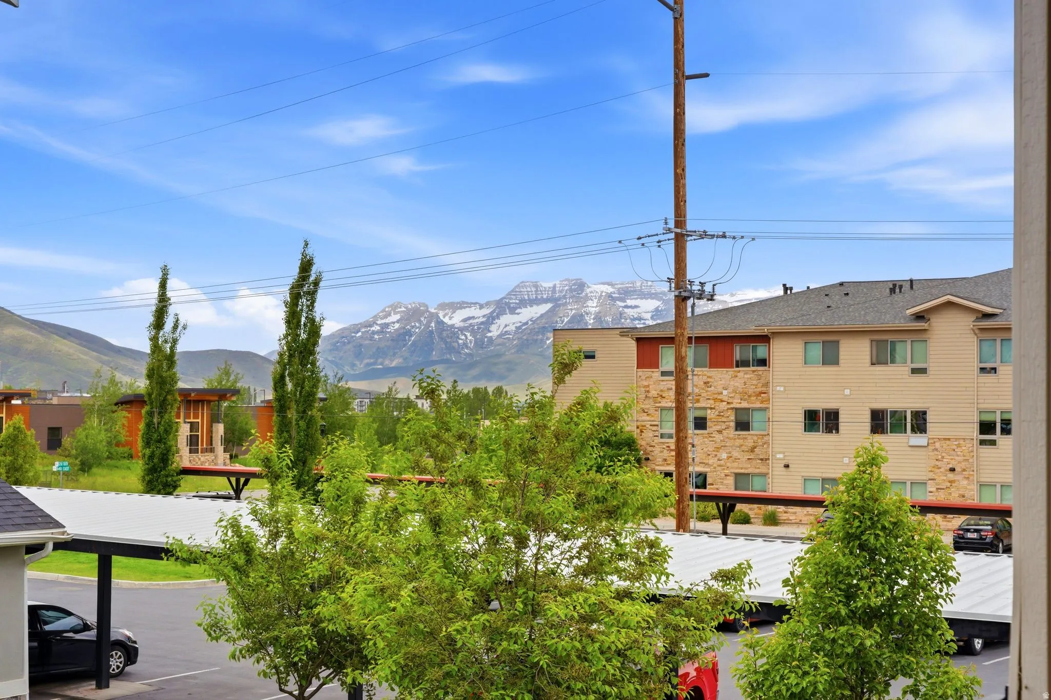 Snow-capped mountains create a striking backdrop for this property, featuring covered parking, mature trees, and a multi-level building with stone and siding facade