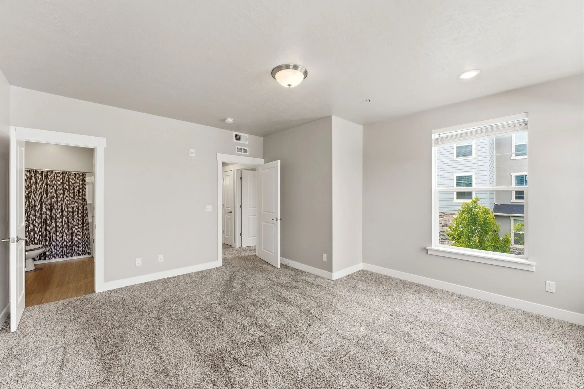 Spacious room featuring light gray walls, plush carpet flooring, and a large window with white blinds