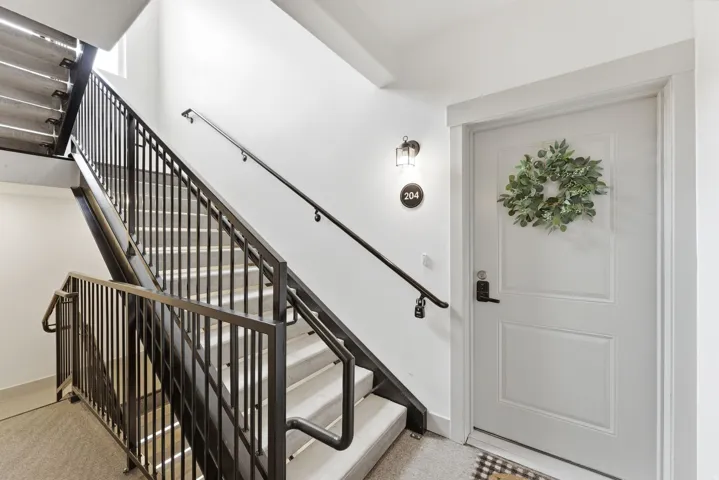 Stairwell featuring metal railings, light-toned stair treads, and a white entry door with panel detailing