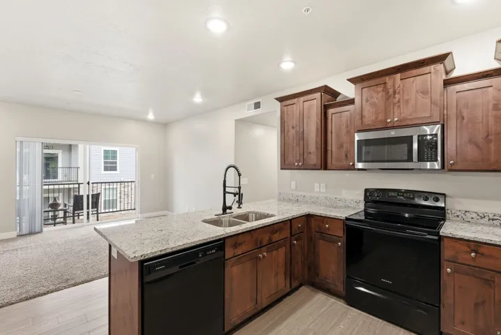 Modern kitchen featuring dark wood cabinetry, light speckled countertops, and stainless steel appliances including an oven, microwave, and dishwasher
