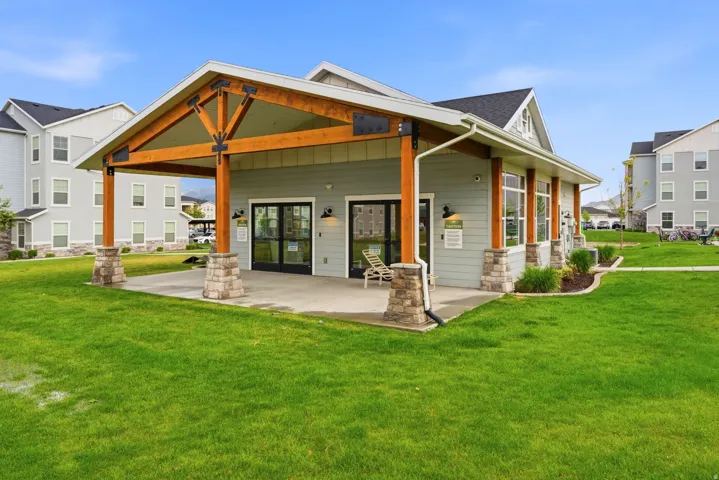 Craftsman-style clubhouse featuring a covered patio, exposed wood beams, stone column bases, and expansive glass doors