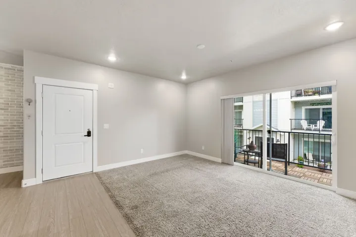 Living area with light gray walls, recessed lighting, and a combination of light wood-finish flooring and gray carpeting