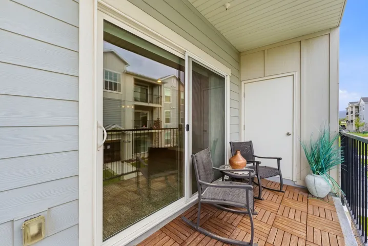 Private balcony featuring wood-finish floor tiles, a sliding glass door, an exterior storage closet, and a black metal railing