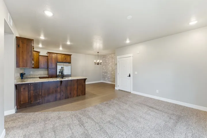 Open concept living space featuring a carpeted area, wood-finish flooring, and a kitchen with wood cabinetry, light-colored countertops, and stainless steel appliances