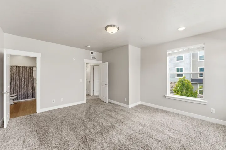 Spacious room featuring light gray walls, plush carpet flooring, and a large window with white blinds