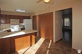 Kitchen featuring wood-finish cabinetry, white appliances, a tile backsplash, and a breakfast bar with a light-colored countertop