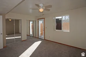 Carpeted interior space featuring a ceiling fan with integrated lighting, two sets of mirrored closet doors, a single-pane window, and a glass-paneled exterior door