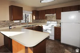Kitchen featuring wood-finish cabinetry, light-toned countertops, a textured tile backsplash, and a window above the sink