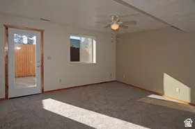 Spacious room featuring neutral wall tones, gray carpeting, a multi-speed ceiling fan with integrated lighting, and a glass-paneled door providing outdoor access