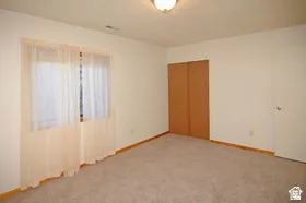 Carpeted room featuring a window with sheer drapes, bi-fold closet doors, a white door with a round knob, wood baseboards, and a ceiling-mounted light fixture