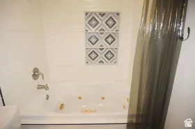 Bathroom featuring a jetted tub, white tile surround, brushed nickel fixtures, and decorative accent tiles