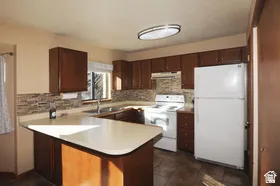 Kitchen featuring wood cabinetry, a breakfast bar, stone-look tile backsplash, and tile flooring