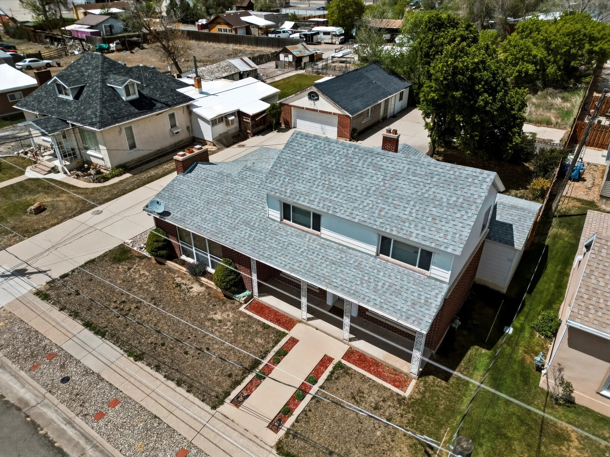 Brick and siding exterior featuring a covered front porch with white columns, a pitched roof with light gray shingles, and a paved driveway leading to a detached garage