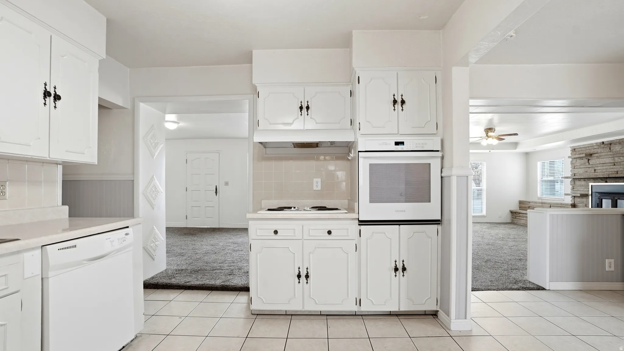 White kitchen featuring tile flooring, white cabinetry with dark hardware, a built-in wall oven, and a white dishwasher