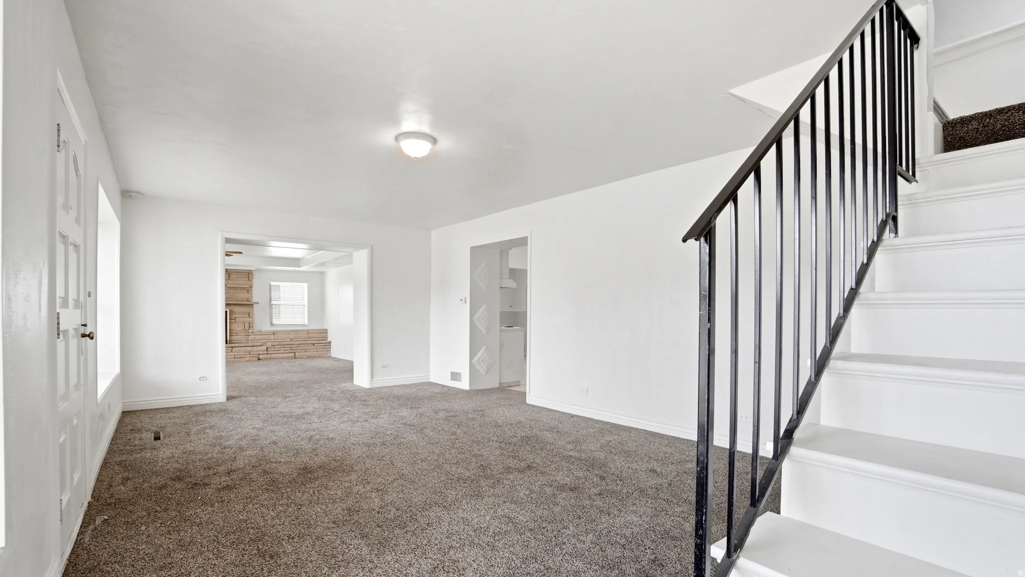 Living area with neutral carpet, white walls, and a staircase featuring a black metal railing
