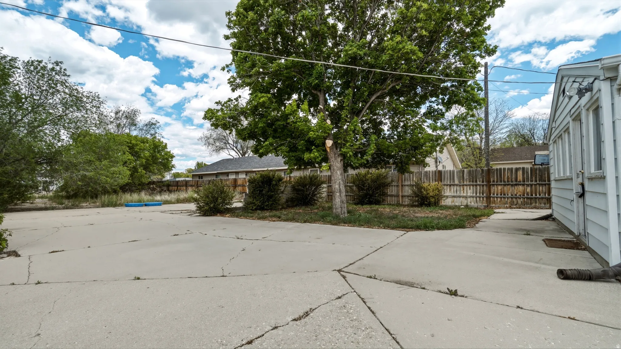Expansive concrete patio area featuring mature trees and established perimeter fencing