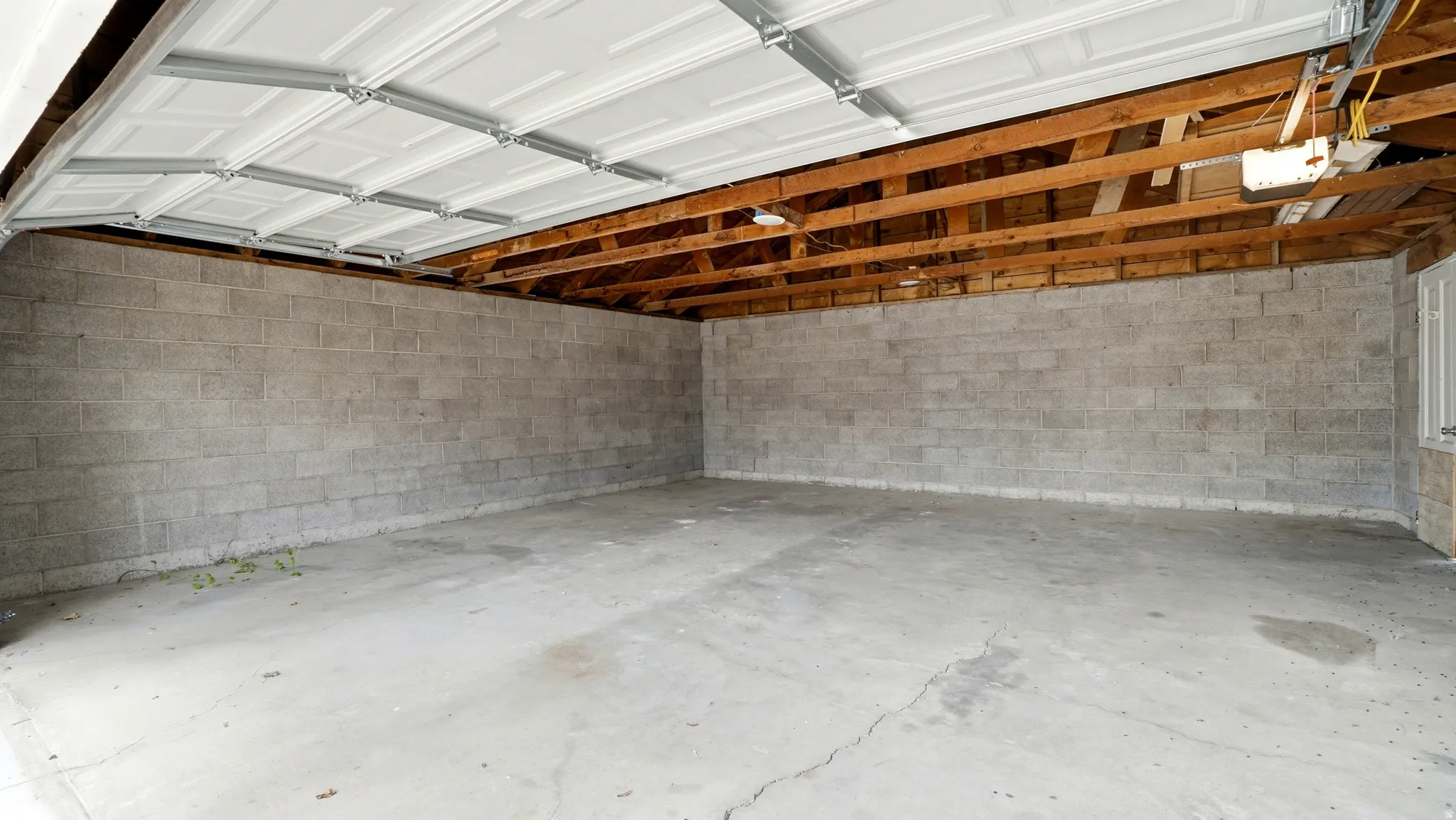 Spacious garage with concrete block walls, exposed wood ceiling joists, and a white paneled overhead door