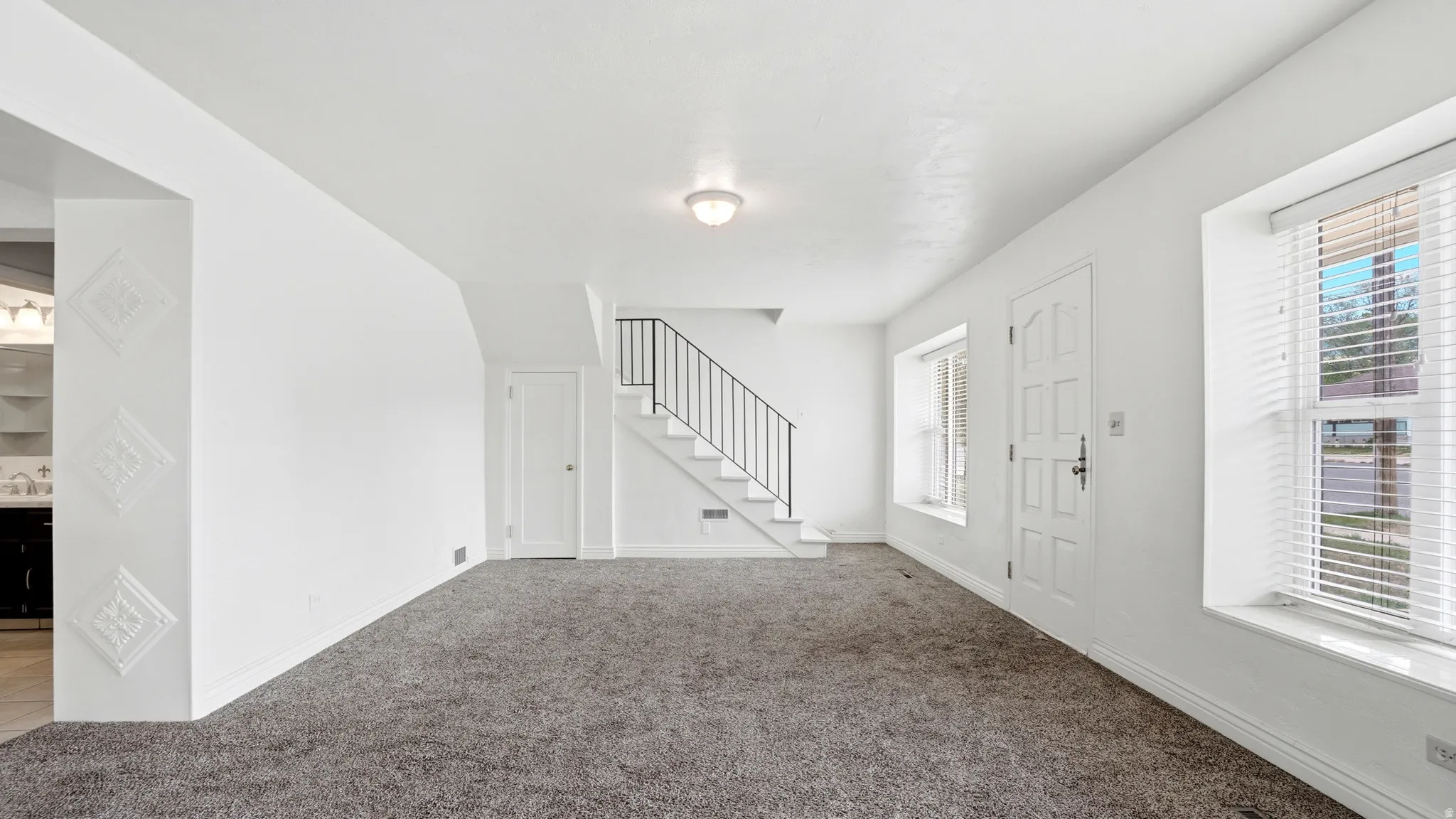 Spacious main room with neutral gray carpeting and white painted walls