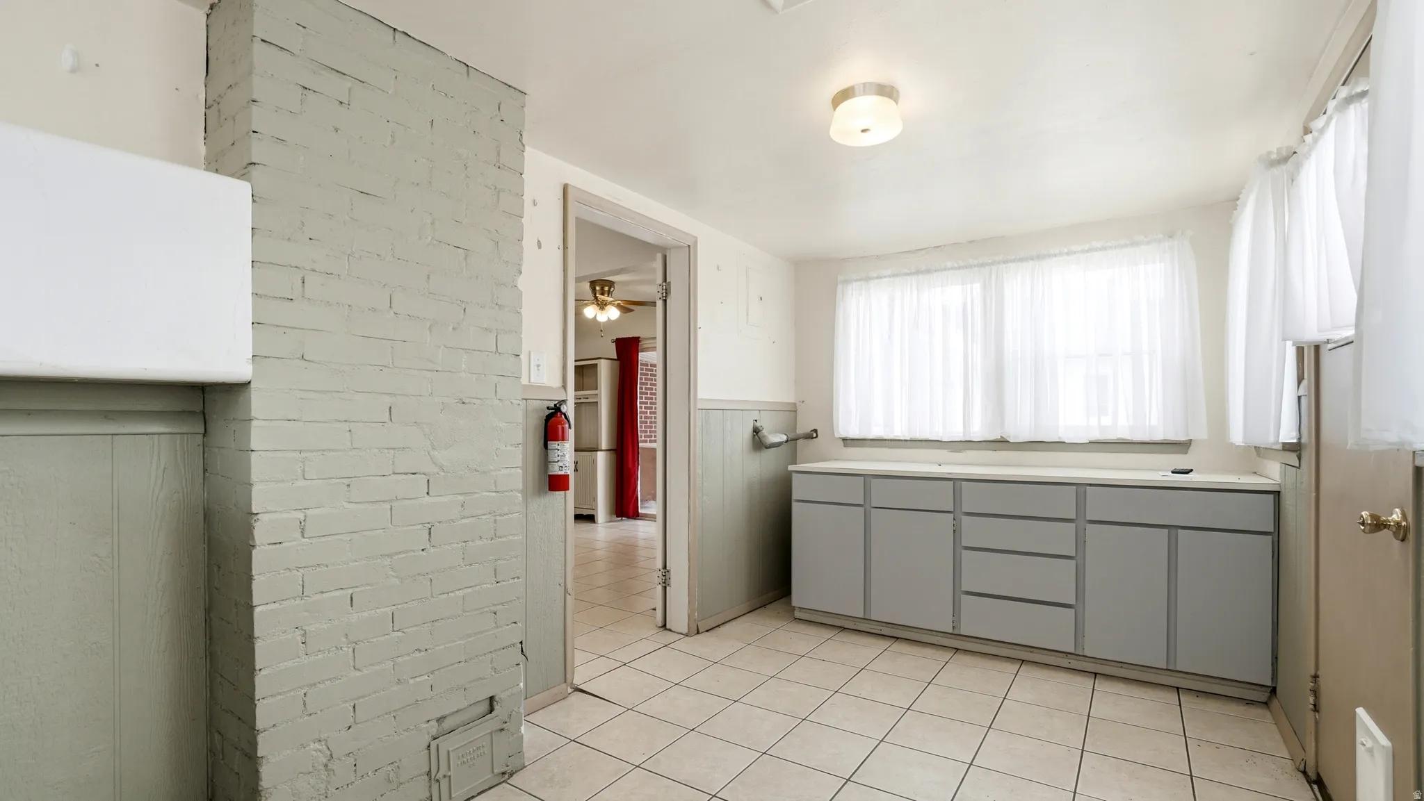 Utility space featuring a painted brick column, light gray base cabinetry with a solid surface countertop, tiled flooring, and a flush mount ceiling fixture