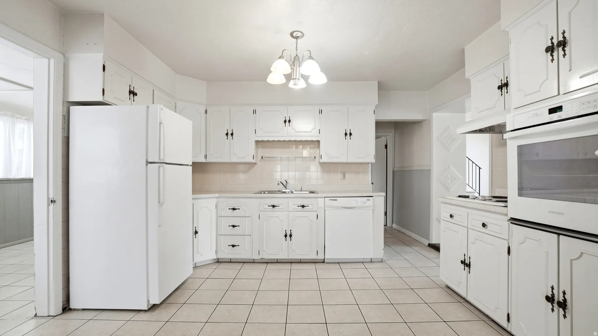 Full kitchen featuring extensive white cabinetry, white tile flooring, built-in wall oven, dishwasher, and a refrigerator