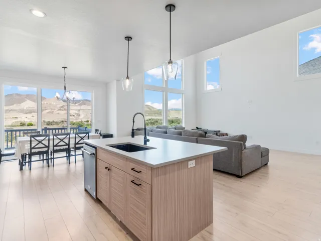 Open-concept living area with light wood-finish flooring, a kitchen island featuring a light countertop and black sink, and a stainless steel dishwasher
