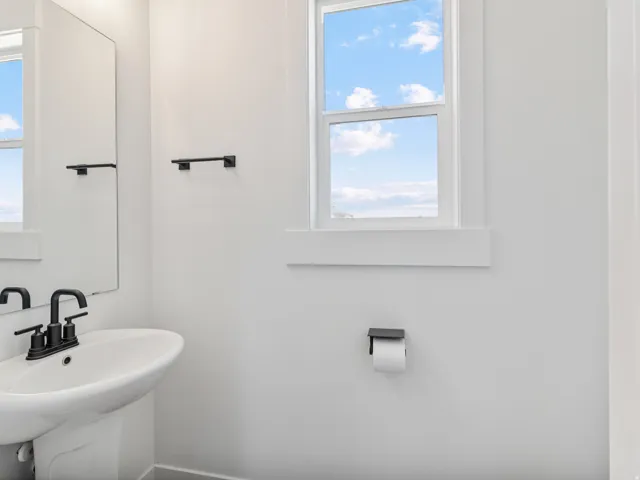 Pedestal sink with matte black faucet, framed mirror, and a window featuring natural light