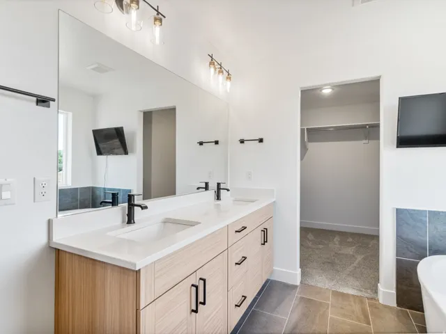 Dual vanity with wood-finish cabinetry, white countertops, integrated sinks, and matte black hardware