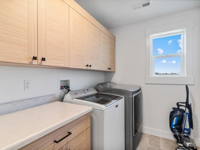 Laundry room featuring wood-finish cabinetry with black hardware, white walls, and a light-colored countertop