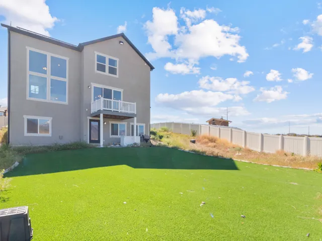Modern stucco exterior with large windows, a second-story balcony, and a ground-level patio