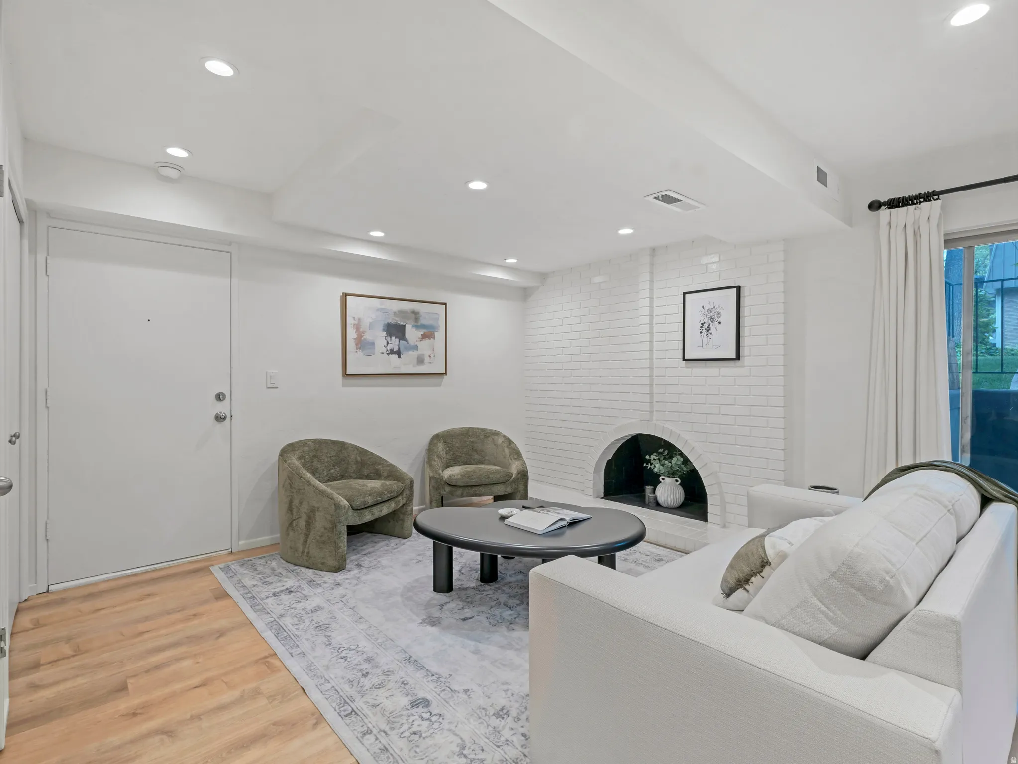 Living area featuring a white brick fireplace with an arched opening, recessed lighting, wood-finish flooring, and a sliding glass door