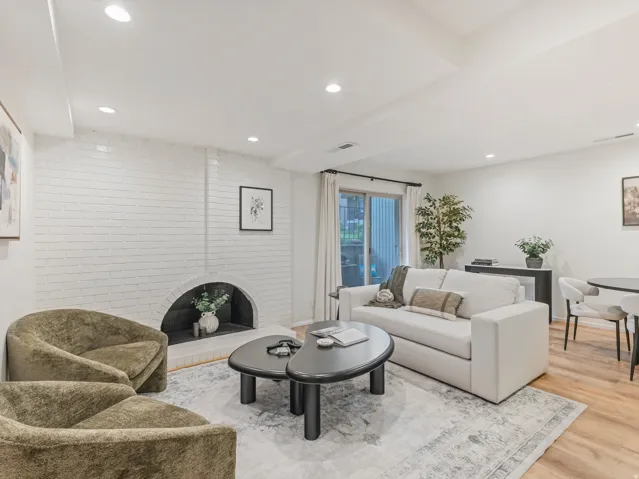 Living space featuring a white painted brick fireplace with an arched opening, recessed lighting, wood-finish flooring, and a sliding glass door