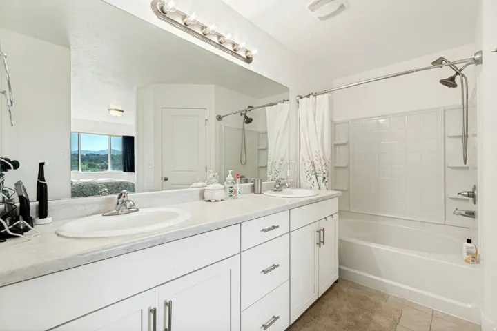 Bathroom featuring a dual vanity with white cabinetry, a single mirror spanning the length of the vanity, and a shower-tub combination with white subway tile surround
