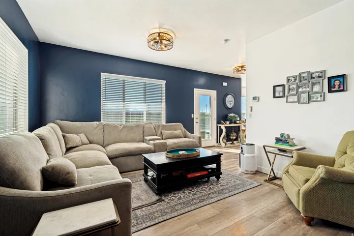 Spacious living area featuring wood-finish flooring, two windows with blinds, and a combination of white and deep blue wall finishes