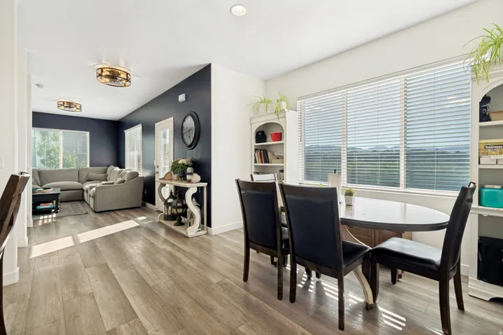 Open-concept living area featuring wood-finish flooring, a contemporary ceiling fan, and a wide window with horizontal blinds