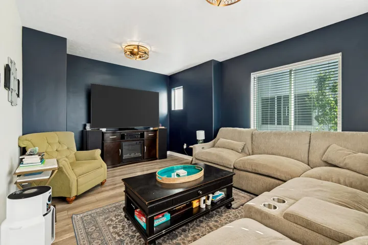 Living area featuring a dark accent wall, wood-finish flooring, and a large window with horizontal blinds