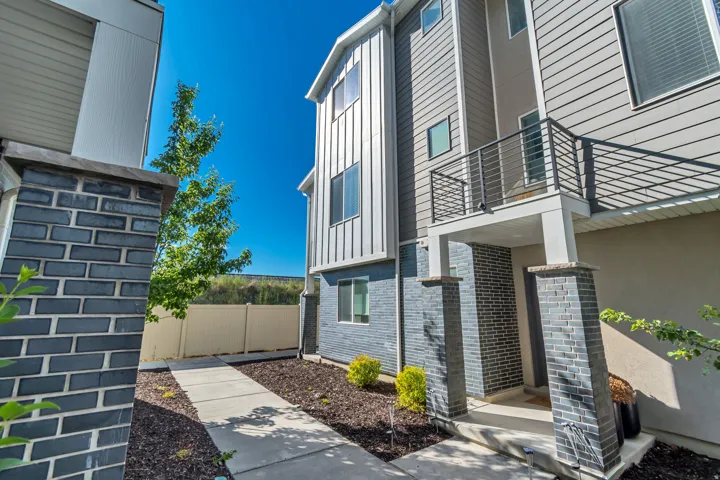 Modern multi-level exterior featuring vertical and horizontal siding, a balcony with a horizontal metal railing, and a covered entry with brick-clad columns