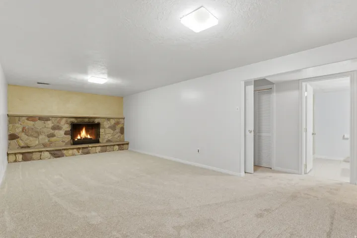 Spacious room featuring a stone-clad fireplace with a hearth, light-toned carpeting, and white walls