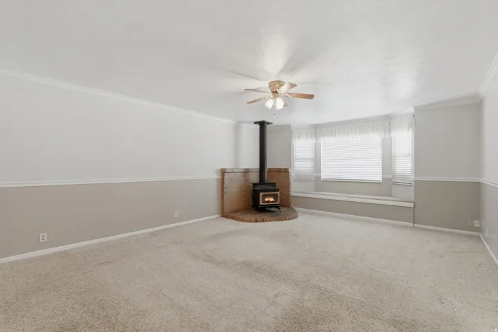 Living area featuring a wood-burning stove with a brick surround, a bay window with integrated bench seating, neutral carpeting, and a ceiling fan