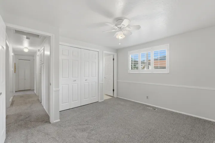 Carpeted interior space featuring white walls and trim, a multi-panel window with white shutters, and a ceiling fan with light fixture